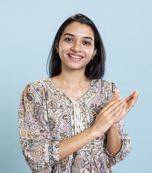 Indian satisfied woman clapping hands and feeling proud of a milestone in studio, pleased and satisfied with an achievement. Smiling adult applauding, saying congratulations for victory.